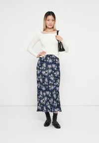 Vit ribbad långärmad topp i kombination med en mörkblommig maxikjol med lila och blå mönster. Svart väska och skor kompletterar outfiten.