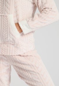 Conjunto de loungewear de felpa en un suave color rosa claro, con un patrón de trenzas texturadas, un forro interior blanco suave y un bolsillo en la parte delantera de la parte superior.