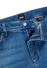 Mėlynos spalvos vidutinio atspalvio džinsai su įprasto kirpimo, užsegami užtrauktuku ir sagomis, kontrastinė siūlė matoma. Matomas prekės ženklas.