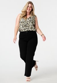 Zwarte broek gecombineerd met een mouwloze blouse met een luipaardprint en een V-hals. Het model draagt lichte, gespsandalen met hakken.