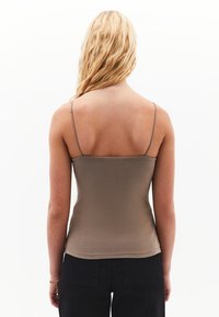 Bruine, aangesloten camisole met dunne bandjes, gladde textuur en een rechte zoom. Gepaard met zwarte broek, wat zorgt voor een eenvoudige en casual uitstraling.