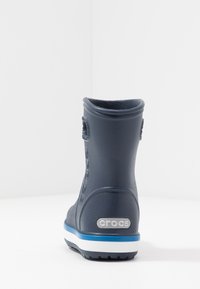 Botte imperméable bleu marine avec une surface texturée, un bout rond et une bande blanche sur la semelle. Présente le logo de la marque sur le talon et à l'arrière.