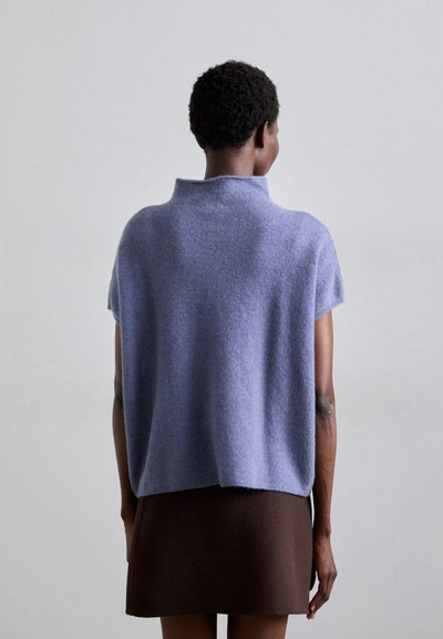 Suéter de punto de manga corta en color lila con cuello alto, hecho de un material suave y texturizado, combinado con una falda ajustada color marrón oscuro.