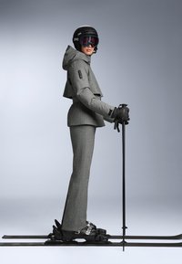 Szürke, textúrált anyagból készült síruha, amely crop kabátot, hozzáillő nadrágot, fekete kesztyűt és árnyékolt szemüveggel ellátott sisakot tartalmaz. Síközlekedéshez sílécek és botok is tartoznak.