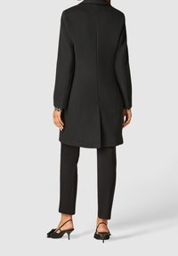 Černý střihaný kabát s dlouhými rukávy a rovný střihem. Nošený přes černé kalhoty a doplněný černými lodičkami s korálkovou ozdobou. Minimální textura.