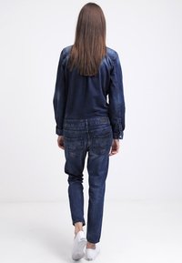 Conjunto de denim que incluye una chaqueta azul oscura de manga larga y unos jeans ajustados a juego. Zapatillas blancas completan el look.