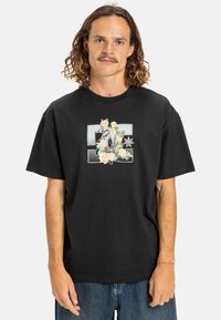 Sort bomulds T-shirt med løs pasform, prydet med et blomstermotiv og stjernedesign i pastelfarver på forsiden. Korte ærmer og rund hals.