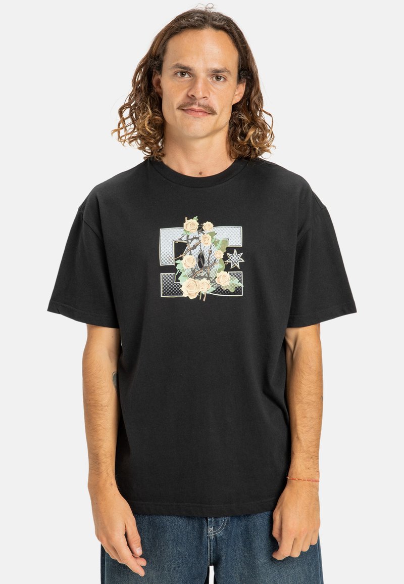 Sort bomulds T-shirt med løs pasform, prydet med et blomstermotiv og stjernedesign i pastelfarver på forsiden. Korte ærmer og rund hals.