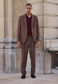 Brown checkered suit with a tailored jacket and matching trousers, layered over a burgundy sweater. Solid black shoes complete the outfit.