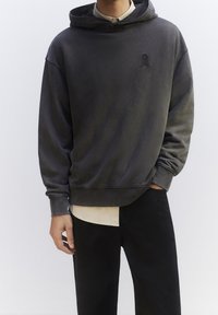 Mikina s kapucí v tmavě šedé barvě, vyrobená z jemného materiálu. Má přední kapsu, žebrované manžety a malé logo na hrudi.