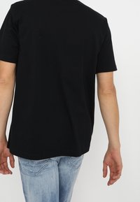 Black cotton t-shirt with a rounded neckline, short sleeves, and a slightly curved hem, paired with light blue denim jeans.