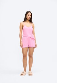 Roosa varrukateta ülikond, mis koosneb ülaosast ja lühikestest pükstest, valminud kergest ja siledast kangast; iseloomulik lõdvestunud istuvus ja elastne vöökoht; sobitatud beežide sussidega.