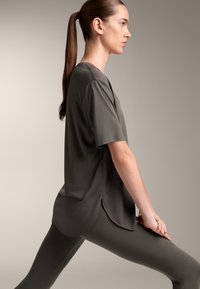 Tummanharmaa lyhythihainen paita pyöreällä helmalla, yhdistettynä samansävyisiin istuviin leggings-housuihin. Sileä pinta ja rento siluetti.