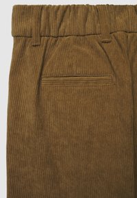 Pantaloni in corduroy marroni con una texture rigata, vita elastica e una singola tasca posteriore con dettaglio di cucitura orizzontale.