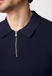 Polo shirt blu navy con un motivo in maglia testurizzata, dotato di colletto corto e chiusura a metà zip con zip in tono dorato.