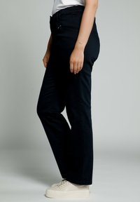 Pantalones de mezclilla negros con un diseño de pierna recta, que presentan una cintura alta y cierre de cremallera. Combinados con zapatillas de plataforma blancas.