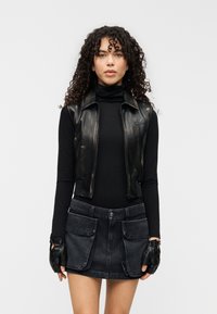 Μαύρο δερμάτινο γιλέκο με ψηλό γιακά, σε συνδυασμό με μαύρη μπλούζα μακρυμάνικη και σκούρα μίνι φούστα από τζιν με μεγάλες μπροστινές τσέπες. Μαύρα γάντια.