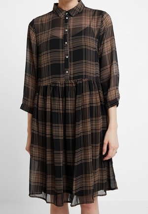 Sukienka w czarno-brązową kratę, zapinana na guziki, z kołnierzykiem, rękawami do połowy przedramienia oraz marszczonym wykończeniem w talii, noszona przez osobę.