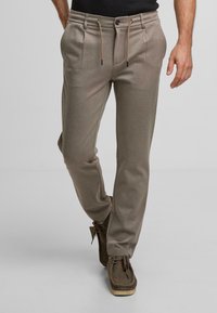 Lichtgrijze sportbroek met binnenband, zijzakken en subtiele plooidetails. Gekocht met donkerbruine schoenen met veters.