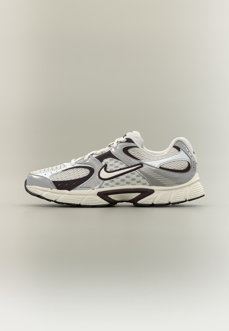 Chaussure de course Nike blanche et grise avec des panneaux en maille, des accents noirs et une semelle coussinée, présentée sur un fond uni.