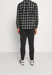 Camicia di flanella a quadri in bianco e nero, con bottoni e maniche lunghe. Abbinata a pantaloni neri affusolati e sneaker in bianco e nero.