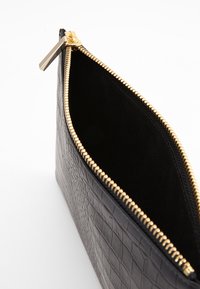 Black crocodile-patterned leather clutch with a gold zipper. The interior is lined with black fabric, showcasing its spacious, open design.