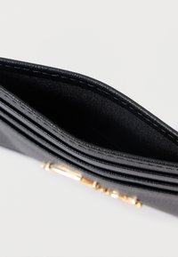 Melnas ādas maks ar vairākiem nodalījumiem un gludu tekstūru; tajā ir zelta toņa aparatūra atveres vietā.