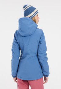 Blaue wasserdichte Jacke mit Kapuze, elastischen Manschetten und taillierter Passform. Getragen mit rosa Hosen, die eine einfache, glatte Textur zeigen.
