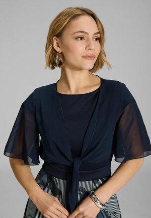 Top a strati blu navy con maniche a farfalla trasparenti, legato in vita, abbinato a una gonna a righe. Tessuto morbido e dettagli delicati.