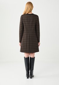 Robe droite noire à motifs avec manches longues, design géométrique et ourlet évasé. Associée à des bottes mi-hautes noires brillantes.