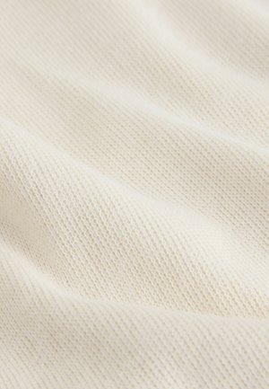 Tessuto in maglia color avorio, caratterizzato da un motivo finemente strutturato con punti visibili e una superficie morbida leggermente rigata.