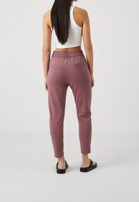 Ljusrosa joggerbyxor med en avsmalnande design, elastisk midja och diskreta sidofickor. Slät tygtouch, i kombination med svarta sandaler.