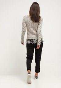 Pull tricoté avec une texture multicolore et un ourlet à franges, porté avec un pantalon noir fuselé et des baskets à motifs. Vue de dos.