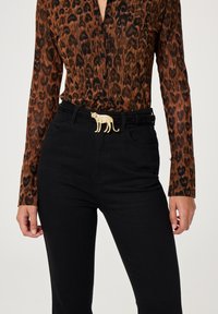 Braune und schwarze Leopardenmuster-Bluse mit langen Ärmeln, kombiniert mit schwarzen Jeans und einer goldenen, katzenförmigen Gürtelschnalle.