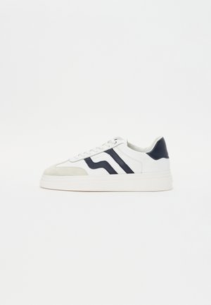 Weißer Sneaker mit Wildleder- und Lederpanelen. Verfügt über navyblaue Streifen, flache weiße Schnürsenkel und eine dicke weiße Sohle.