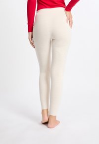 Leggings beiges con una textura suave y un diseño ajustado, que presentan una cintura alta y un acabado sin costuras, usados descalzos sobre un fondo liso.
