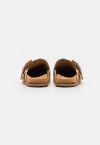 Rjave semiš slip-on čevlje z odprtim zadnjem delom, ki imajo dekorativne verižne dodatke na zgornjem delu in ravno, teksturirano podplato.