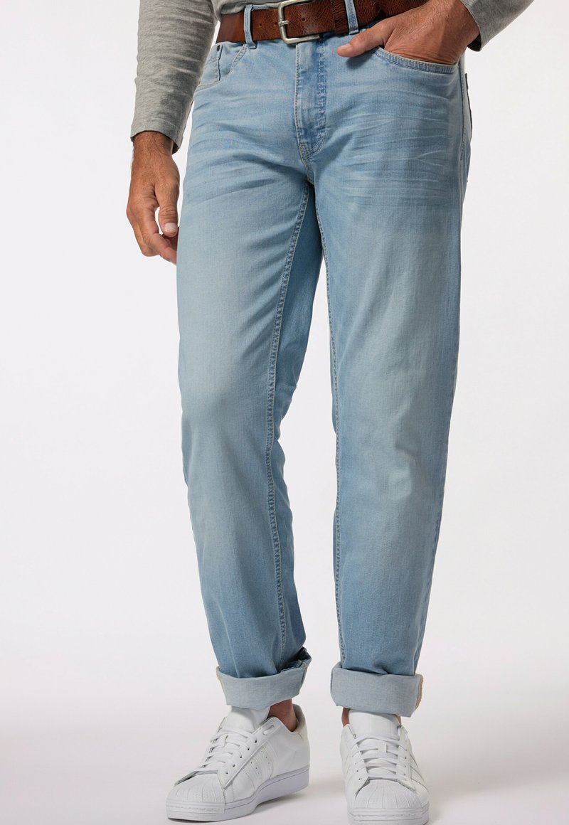 Celana denim biru muda dengan potongan santai, ujung yang digulung, dan saku depan. Dipasangkan dengan sepatu sneakers putih dan atasan lengan panjang berwarna abu-abu.