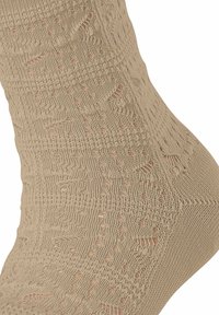 Beige gemusterte Socke mit strukturiertem Strick, die offene Maschen und unterschiedliche Stichmuster für Atmungsaktivität und Komfort aufweist.