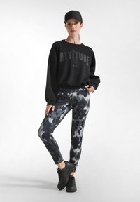 Černý zkrácený svetr s textem "ATTITUDE", doplněný o úzké legíny s černobílým tie-dye vzorem. Černé tenisky outfit dokončují.