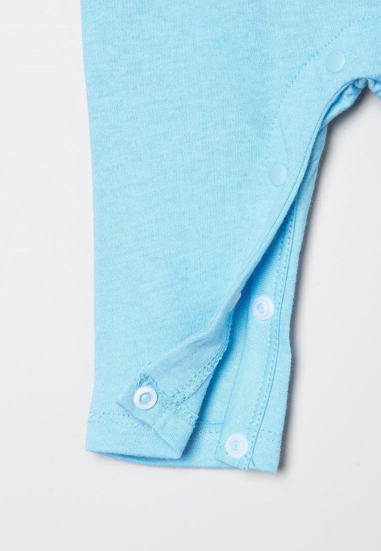 Combinaison en tissu bleu clair avec des manches courtes, dotée de boutons pression sur le côté pour un habillage facile. Texture douce, design simple.
