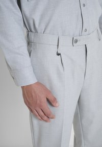 Lichtgrijze, gestructureerde broeken met voorplooien, knoopsluiting en een verstelbare tailleband. Gecombineerd met een bijpassende blouse met lange mouwen.