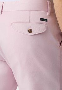 Světle růžové kalhoty z bavlny, s kapsou na zadní straně s klopou, zapínáním na knoflík a malou značka na kapse.
