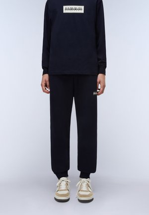 Black long-sleeve shirt with rectangular logo, paired with matching sweatpants featuring a small logo. White and beige sneakers complete the look.
