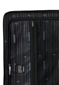 Black suitcase interior with zippered compartments, featuring a graphic pattern of airplanes and runway lines. Brand label visible.