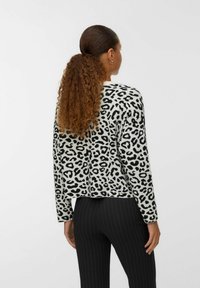 Pull en imprimé léopard noir et blanc, à manches longues et design court. Tissu doux, vu de dos, associé à un pantalon noir à rayures.