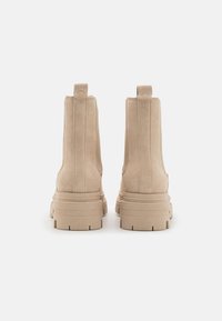 Beige Wildleder-Stiefeletten mit einer robusten Sohle und einem inklusiven Absatz. Mit hinterem Zugband und vertikalen Nähten an den Seiten.