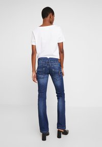 Tummansiniset farkut, joissa lievä levenemä, kaksi takataskua, ommeltu kuvio ja ruskea nahkainen merkki vyötäröllä.