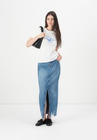 Hvid t-shirt med blå skaldgrafik, parret med en lys blå denimnederdel med slids foran og frayed kant, samt en sort taske.