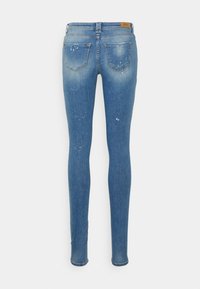 Jeans skinny de ganga azul com um efeito desbotado, apresentando marcas de desgaste e detalhes de respingos. Projetados com bolsos traseiros e uma cintura padrão.